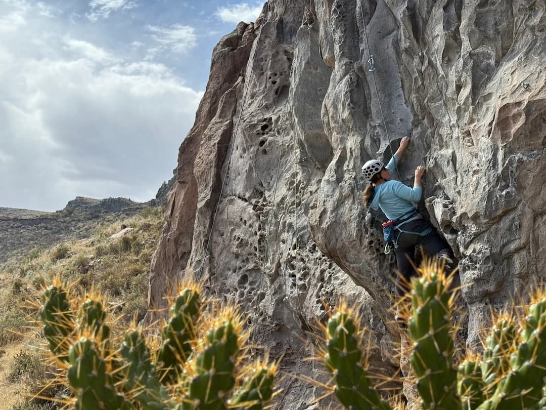 A climber on a rock wall overlooking the mountain landscape in Peru.