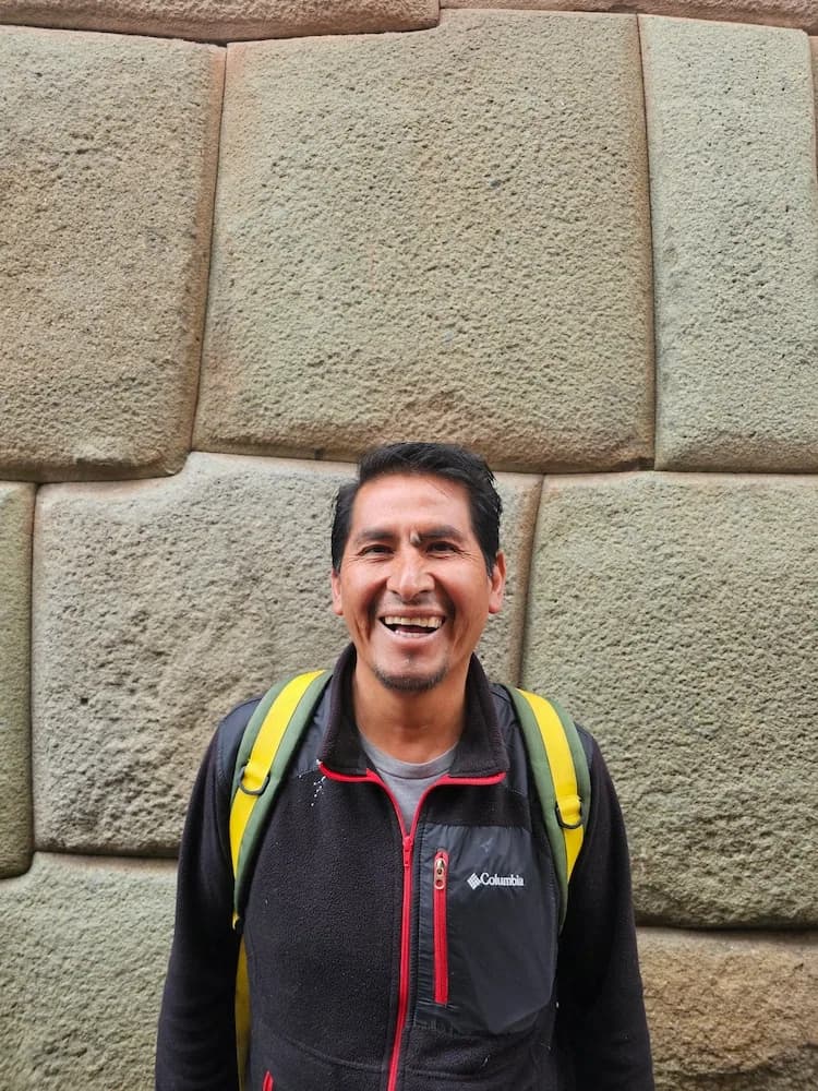Portrait of Vidal Jaquehua smiling in front of Inca stonework in Cusco.